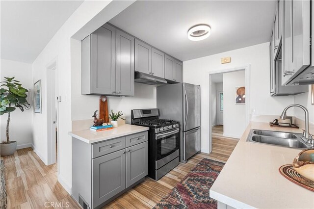 kitchen featuring stainless steel range with gas cooktop, light wood-style flooring, a sink, gray cabinetry, and under cabinet range hood