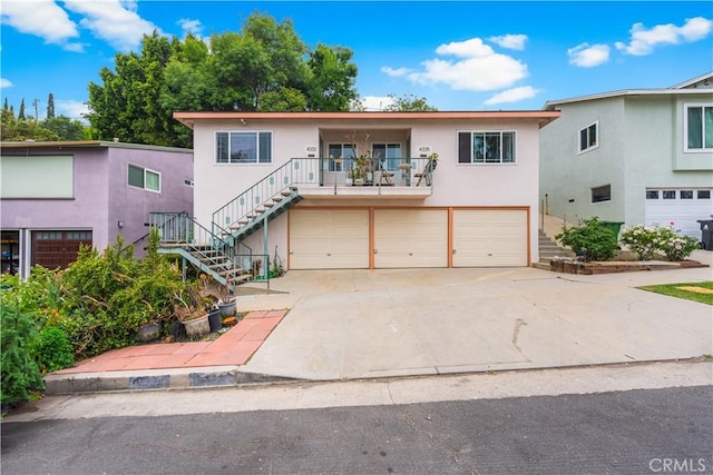 front facade with a garage, stairway, stucco siding, and concrete driveway