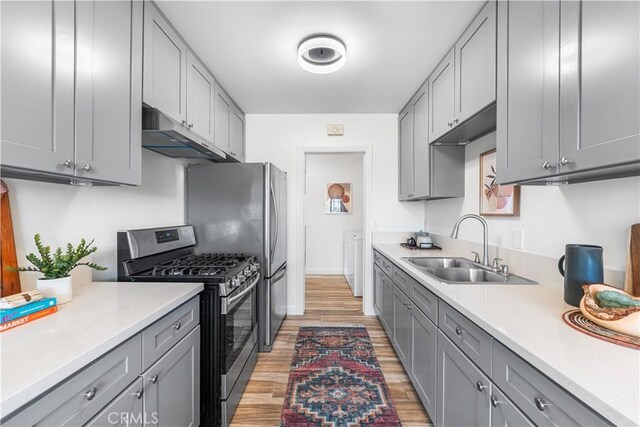 kitchen with a sink, under cabinet range hood, stainless steel gas range, light wood finished floors, and gray cabinets