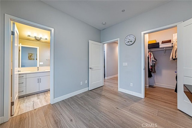 unfurnished bedroom featuring light wood finished floors, a sink, baseboards, connected bathroom, and a walk in closet