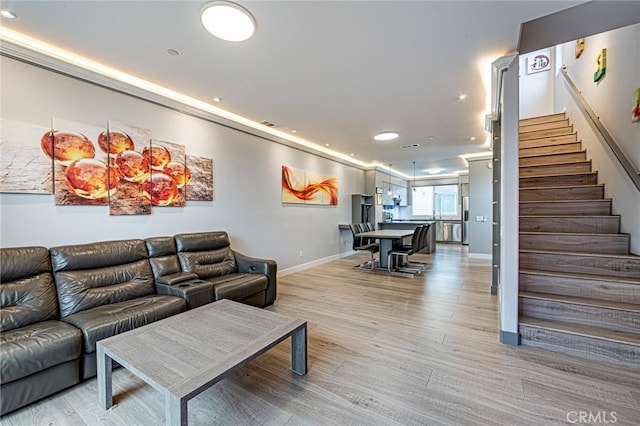 living room featuring light wood-style flooring, baseboards, recessed lighting, and stairway