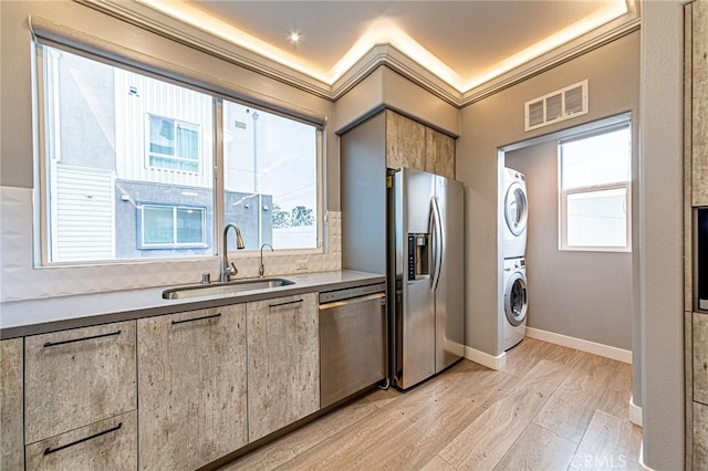 kitchen featuring stainless steel appliances, a sink, visible vents, stacked washer / dryer, and light wood-style floors
