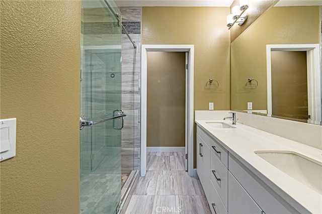 full bath featuring a textured wall, a sink, a shower stall, and double vanity