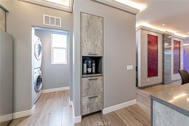 clothes washing area featuring stacked washer and dryer, light wood-style flooring, visible vents, baseboards, and laundry area