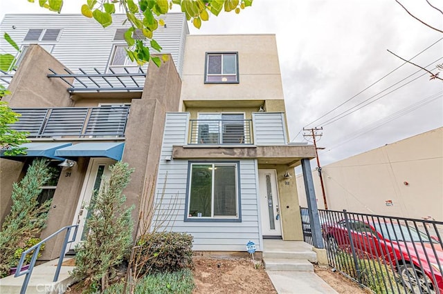 view of front of home with stucco siding, a balcony, and fence