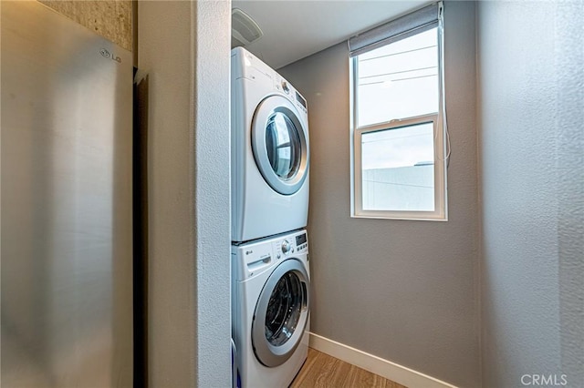 laundry area with baseboards, stacked washer and dryer, laundry area, and light wood-type flooring