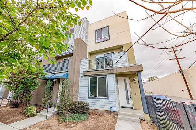 view of front of home with fence, a balcony, and stucco siding