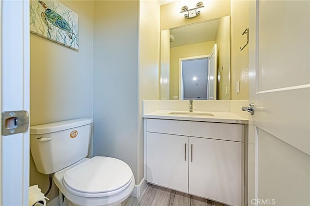 half bathroom with baseboards, wood finished floors, vanity, and toilet