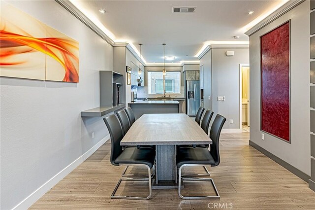 dining room featuring light wood-style flooring, visible vents, baseboards, and ornamental molding