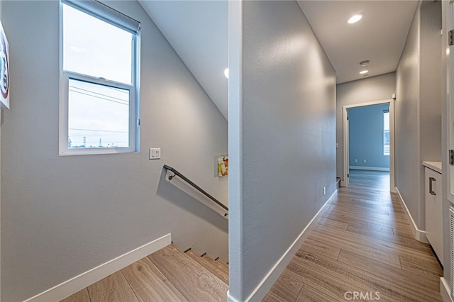 hallway with baseboards, an upstairs landing, and light wood-style floors