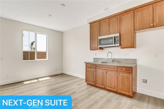 kitchen with a sink, baseboards, light stone counters, stainless steel microwave, and light wood-style floors