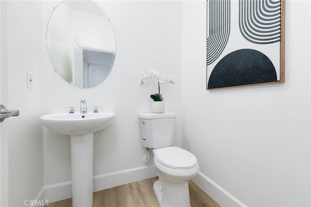 half bath with toilet, baseboards, a sink, and wood finished floors