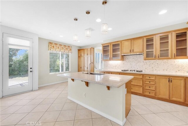 kitchen with light tile patterned flooring, light stone countertops, a sink, tasteful backsplash, and a center island with sink
