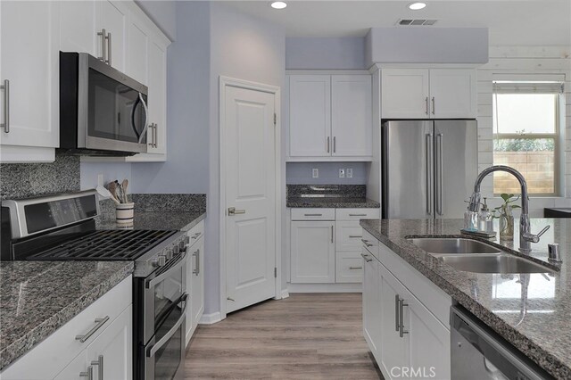 kitchen featuring appliances with stainless steel finishes, light wood-type flooring, a sink, white cabinetry, and visible vents