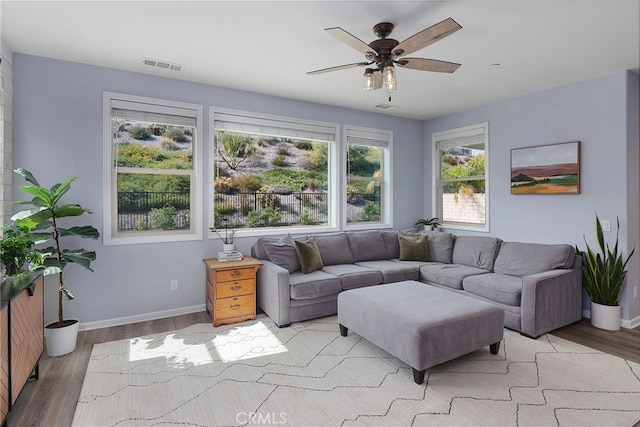 living area with baseboards, visible vents, ceiling fan, and light wood finished floors