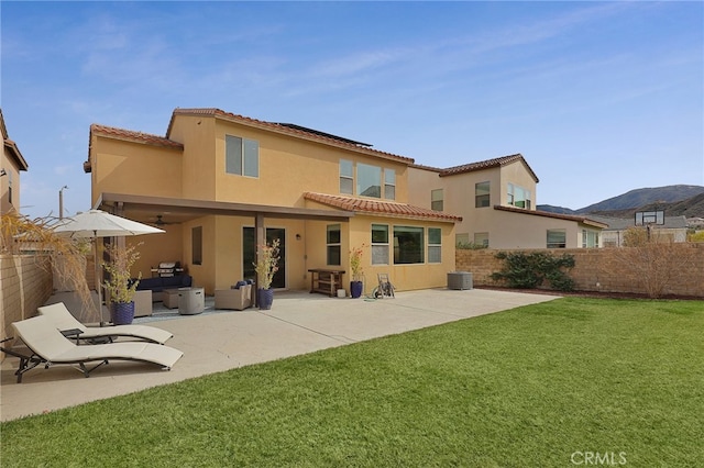 back of house with stucco siding, a yard, a fenced backyard, and a tile roof