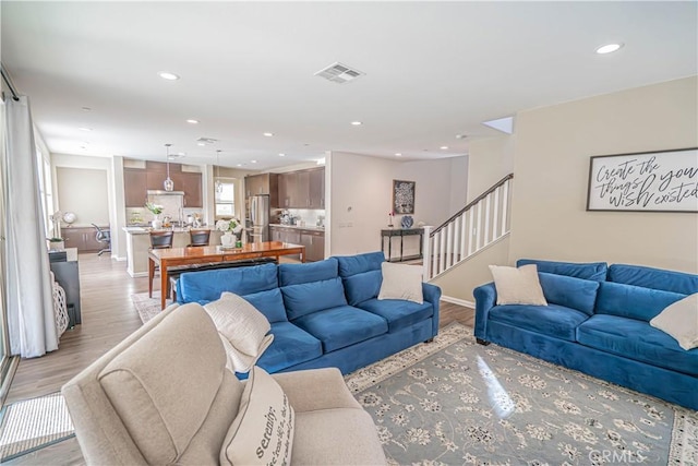 living area with recessed lighting, light wood-type flooring, stairs, visible vents, and baseboards