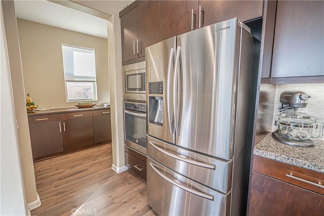 kitchen with dark brown cabinetry, light wood-style flooring, stainless steel appliances, and decorative backsplash