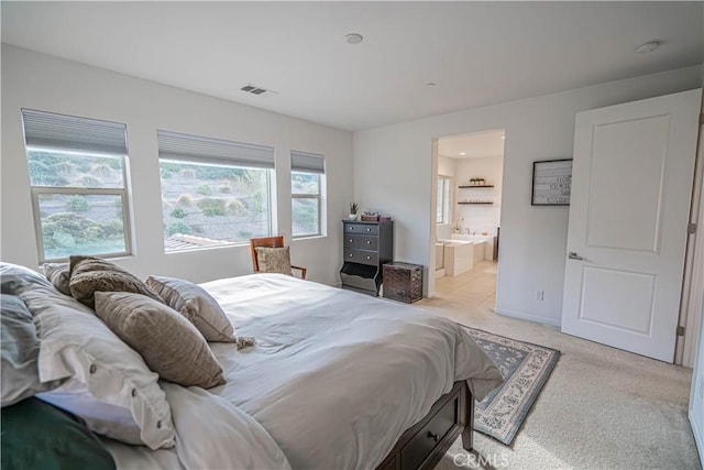 bedroom with baseboards, visible vents, light carpet, and ensuite bath