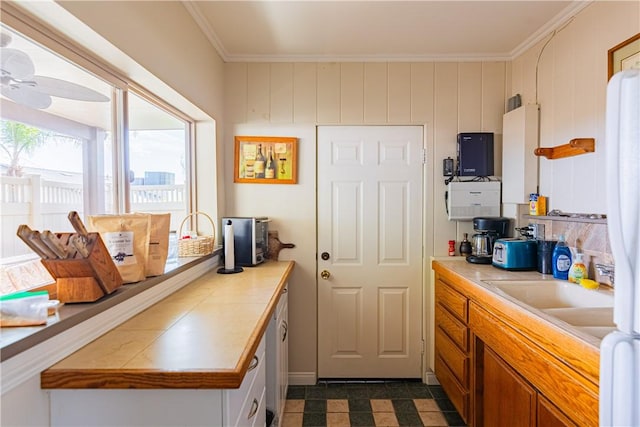kitchen featuring a sink, ceiling fan, light countertops, ornamental molding, and brown cabinetry