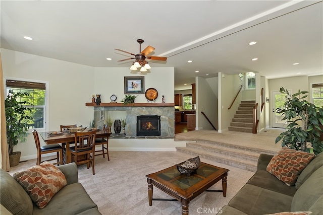 living area featuring recessed lighting, a warm lit fireplace, stairs, baseboards, and light colored carpet