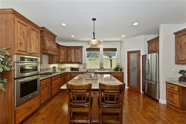 kitchen featuring light stone countertops, decorative backsplash, dark wood-type flooring, a kitchen island, and appliances with stainless steel finishes
