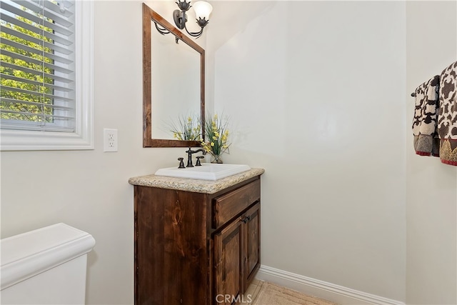 half bathroom featuring baseboards, toilet, and vanity