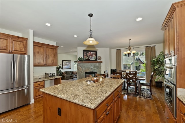 kitchen with light stone counters, appliances with stainless steel finishes, brown cabinets, dark wood-style floors, and a center island