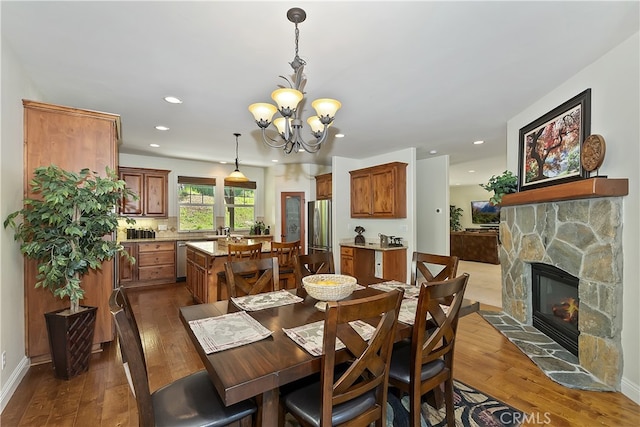 dining space featuring recessed lighting, a notable chandelier, a stone fireplace, and hardwood / wood-style flooring