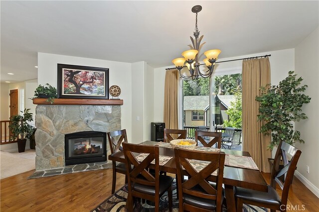 dining room with wood finished floors, a notable chandelier, a stone fireplace, and baseboards