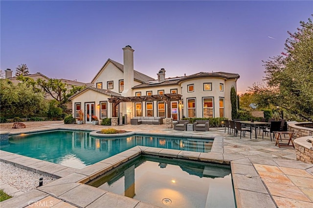 back of property at dusk with an outdoor hangout area, a patio area, an in ground hot tub, and an outdoor pool