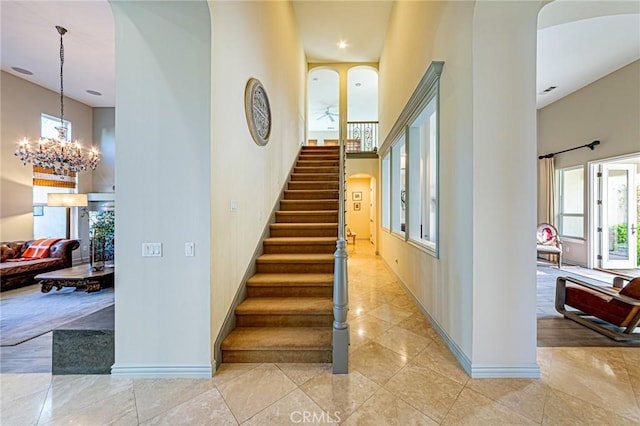 stairway with a towering ceiling, a chandelier, a healthy amount of sunlight, and baseboards