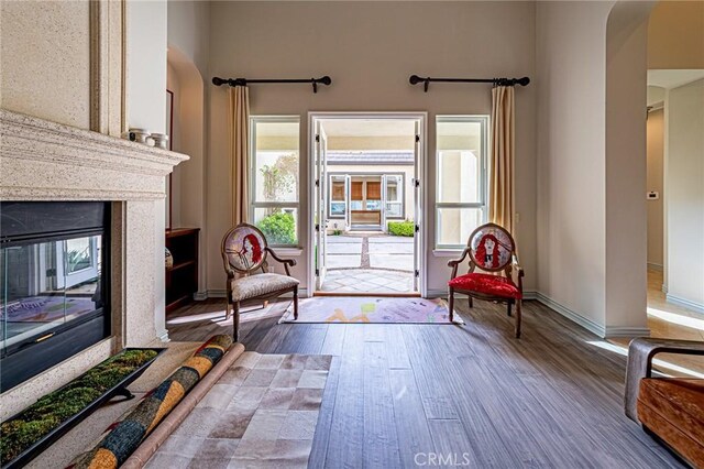 sitting room with wood finished floors, arched walkways, a premium fireplace, and baseboards