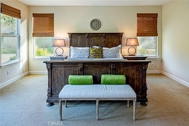 bedroom with multiple windows, light carpet, and baseboards