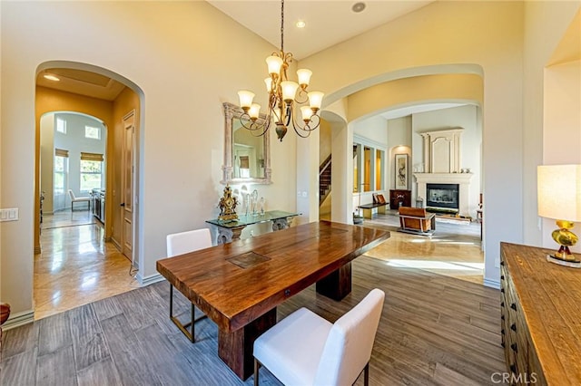 dining area with arched walkways, an inviting chandelier, a glass covered fireplace, dark wood-style flooring, and stairs