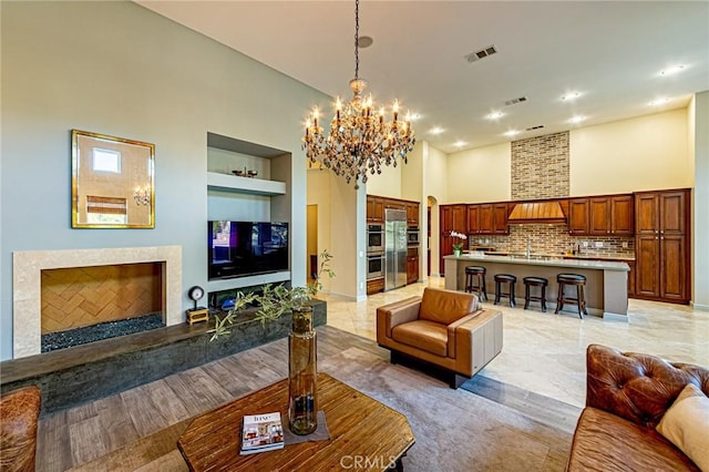 living room featuring an inviting chandelier, built in features, visible vents, a high end fireplace, and a towering ceiling