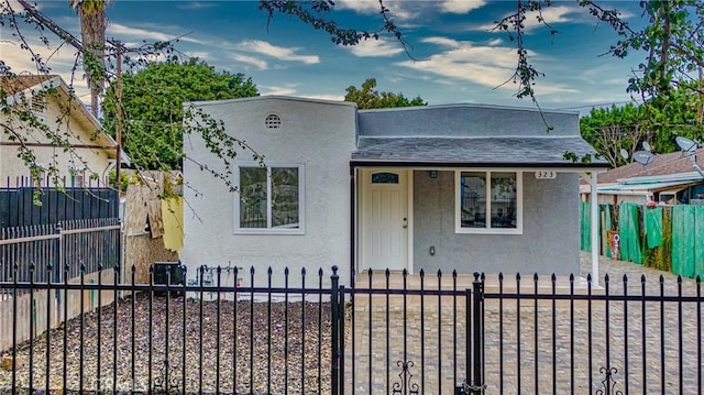 view of front facade with stucco siding, a fenced front yard, and roof with shingles
