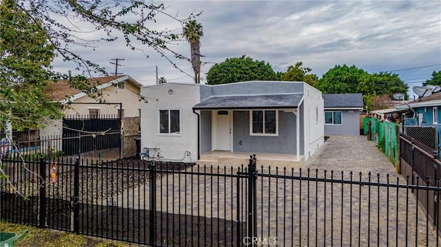 bungalow with covered porch, stucco siding, and a fenced front yard
