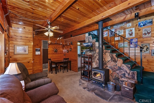 carpeted living room with wood walls, a ceiling fan, a wood stove, and wooden ceiling