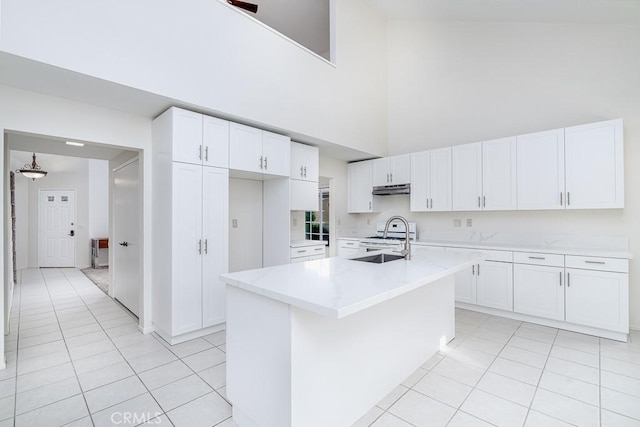 kitchen featuring light tile patterned floors, a sink, under cabinet range hood, and a high ceiling