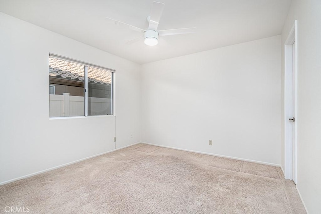 spare room featuring a ceiling fan, light carpet, and baseboards
