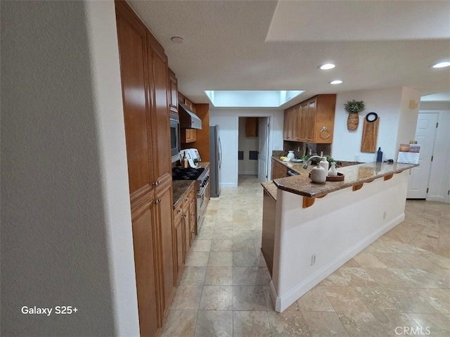 412 Arenoso Ln Unit 102, San Clemente, CA 92672 - kitchen with stainless steel appliances, a kitchen bar, backsplash, a peninsula, and brown cabinets