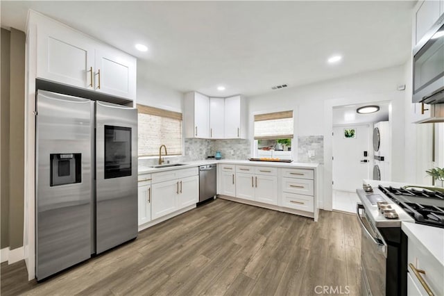 kitchen with white cabinets, appliances with stainless steel finishes, a sink, stacked washing maching and dryer, and wood finished floors