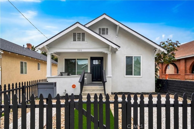 bungalow-style house with a porch, a fenced front yard, and stucco siding