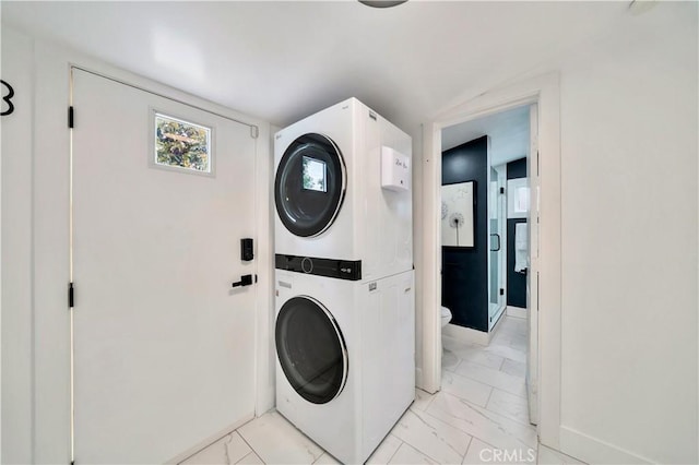 clothes washing area featuring baseboards, laundry area, stacked washer / dryer, and marble finish floor