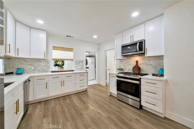 kitchen featuring visible vents, tasteful backsplash, white cabinets, stainless steel appliances, and light wood-style flooring