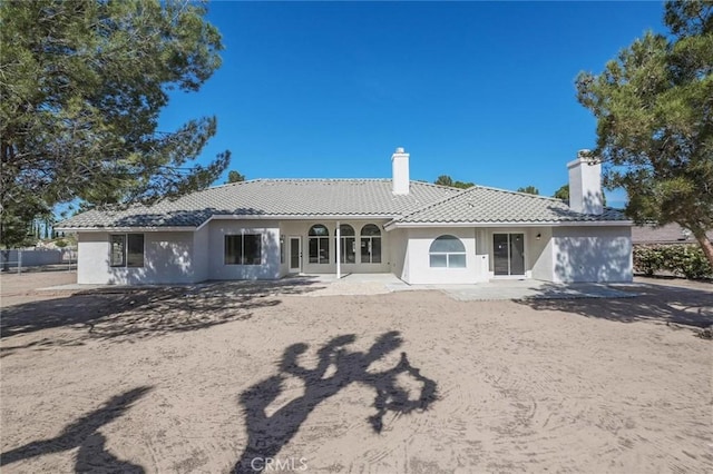 rear view of property with stucco siding, fence, a chimney, and a tile roof