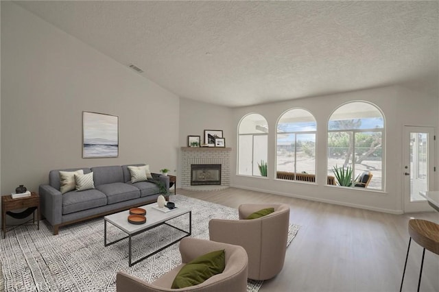 living area with visible vents, wood finished floors, a textured ceiling, and a brick fireplace