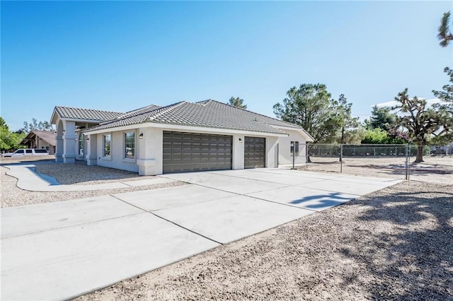 view of side of home with a tile roof, an attached garage, concrete driveway, stucco siding, and fence