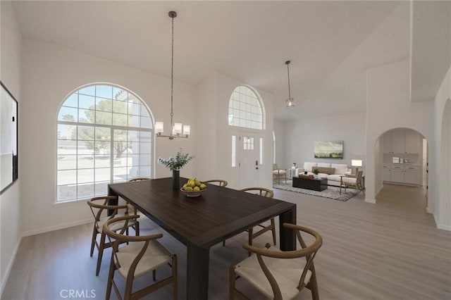 dining room with arched walkways, an inviting chandelier, light wood-style flooring, and baseboards